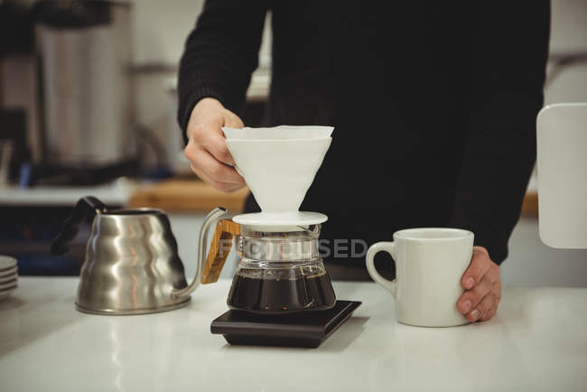 Mid-section of man holding filter funnel and coffee mug in coffee shop — Stock Photo