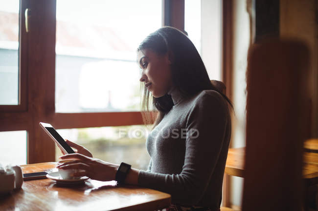 Donna che utilizza tablet digitale mentre prende una tazza di caffè nel caffè — Foto stock