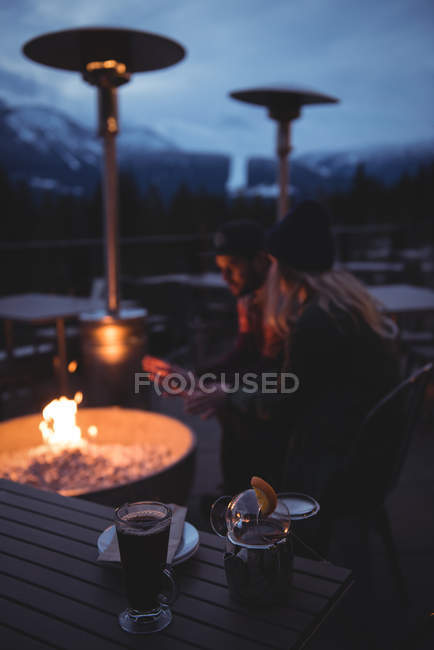 Pareja sentada junto al fuego al atardecer durante el invierno - foto de stock