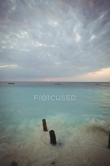 Vieux poteaux en bois dans la mer pendant le coucher du soleil — Photo de stock