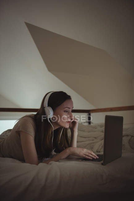 Женщина в наушниках с ноутбуком на кровати дома — стоковое фото