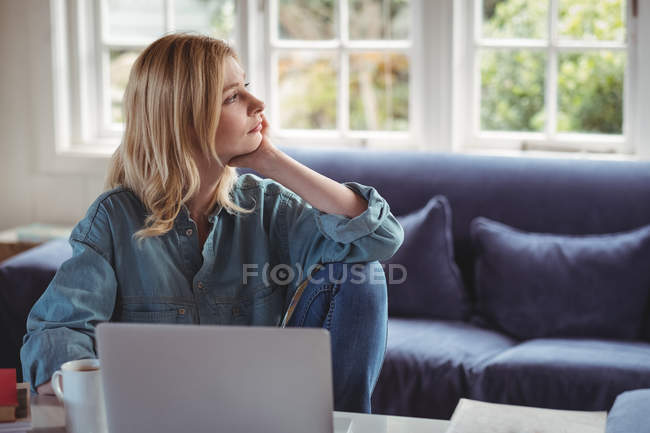 Задумчивая женщина использует ноутбук в гостиной на дому — стоковое фото