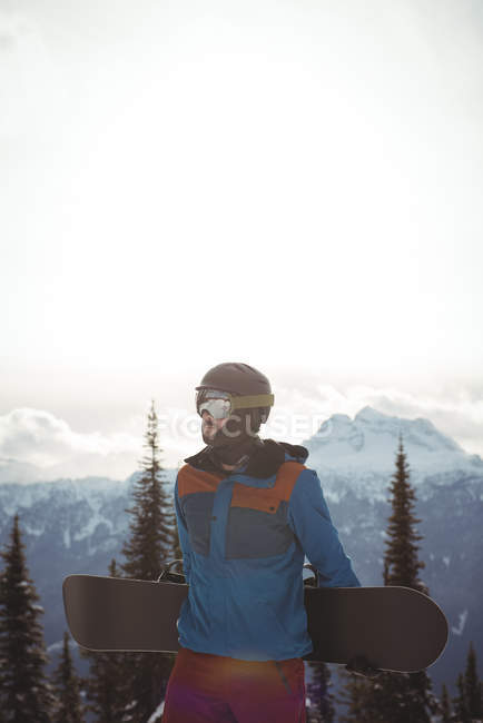 Man holding snowboard against snow capped mountain — Stock Photo