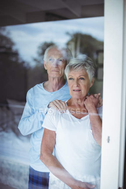 Senior couple looking through window at home — Stock Photo