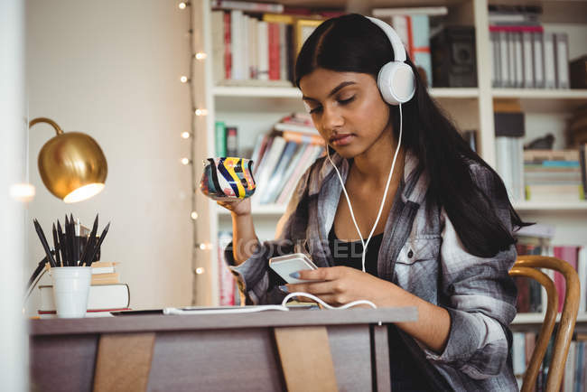 Жінка слухає музику на цифровому планшеті, маючи каву у вітальні вдома — стокове фото