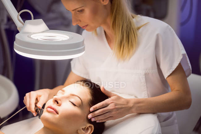Женщина-дерматолог проводит лазерную эпиляцию лица пациента в клинике — стоковое фото