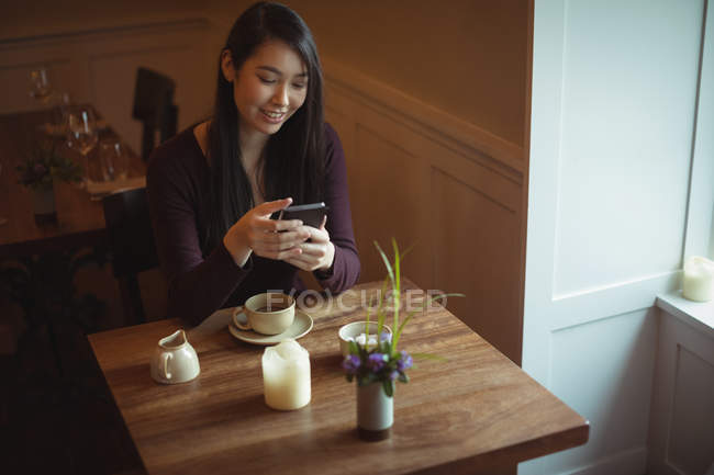Mujer sonriente usando el teléfono móvil en la cafetería - foto de stock