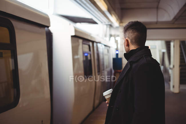 Uomo d'affari con una tazza di caffè usa e getta in attesa di treno sulla piattaforma — Foto stock