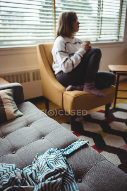 Femme réfléchie assise sur une chaise de canapé dans le salon à la maison — Photo de stock