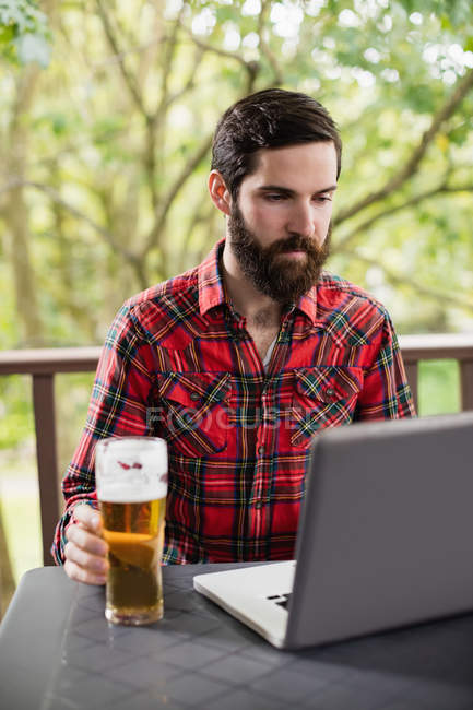 Uomo che utilizza il computer portatile con vetro di birra sul tavolo nel bar — Foto stock