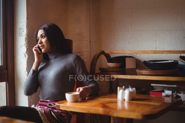 Жінка розмовляє на мобільному телефоні, маючи чашку кави в кафе — стокове фото