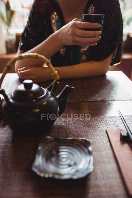 Sección media de la mujer sentada en la mesa y tomando té - foto de stock
