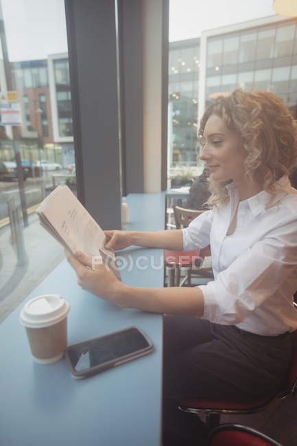 Thoughtful businesswoman reading newspaper at counter in cafeteria — Stock Photo