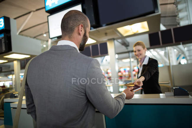 Asistente de facturación de la aerolínea que da pasaporte al viajero en el mostrador en la terminal del aeropuerto - foto de stock