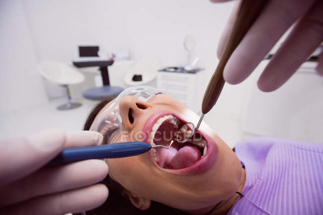 Dentista examinando paciente feminina com ferramentas na clínica odontológica — Fotografia de Stock