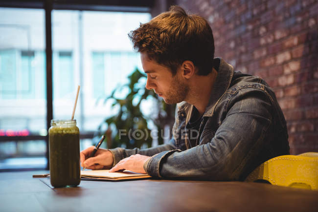 Hombre escribiendo en lácteos con jugo en la mesa en la cafetería - foto de stock