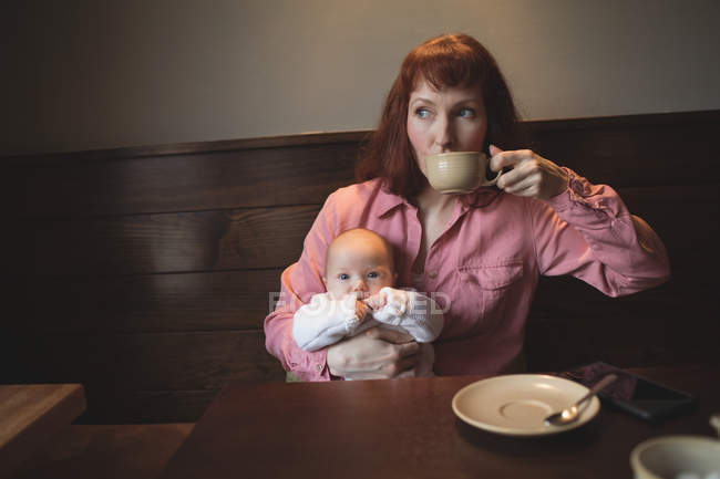 Mãe tomando café enquanto segurando bebê bonito no café — Fotografia de Stock