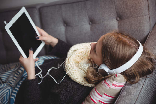 Женщина лежит на диване и слушает музыку на цифровом планшете дома — стоковое фото