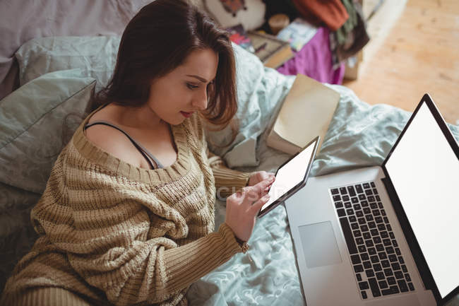 Женщина пользуется цифровым планшетом и ноутбуком на кровати дома — стоковое фото