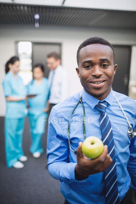 Портрет усміхненого лікаря, який тримає зелене яблуко в лікарняному коридорі — стокове фото