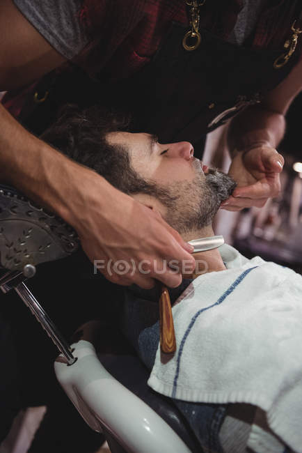 Man getting beard shaved with razor in barber shop — Stock Photo
