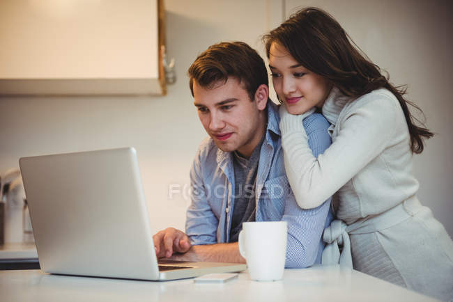 Casal usando laptop enquanto toma café na cozinha em casa — Fotografia de Stock