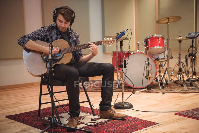 Homem sentado na cadeira e tocando guitarra no estúdio de música — Fotografia de Stock