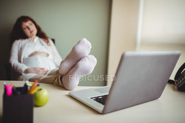 Grávida empresária relaxante com os pés no escritório — Fotografia de Stock