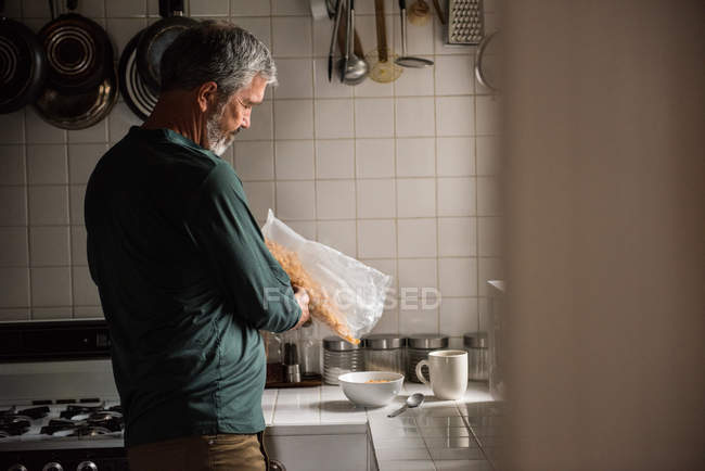 Hombre vertiendo cereales en un tazón en casa - foto de stock