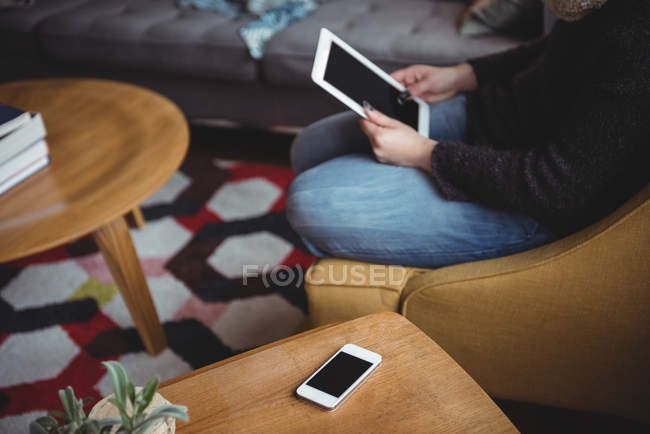 Sección media de la mujer que usa tableta digital en la sala de estar en casa - foto de stock