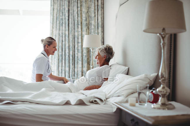 Krankenschwester interagiert mit Seniorin auf Bett im Schlafzimmer — Stockfoto