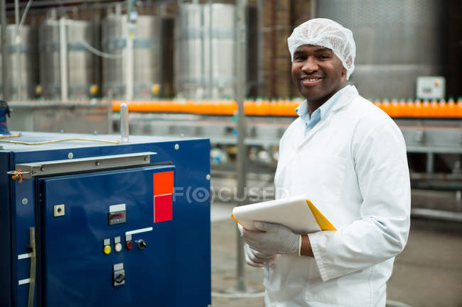 Trabajador masculino sonriente con el portapapeles parado por la máquina en la fábrica del jugo - foto de stock