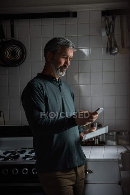 Uomo che utilizza il telefono cellulare in cucina a casa — Foto stock