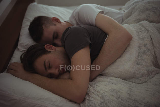 Gay pareja abrazando mientras durmiendo en cama en dormitorio - foto de stock