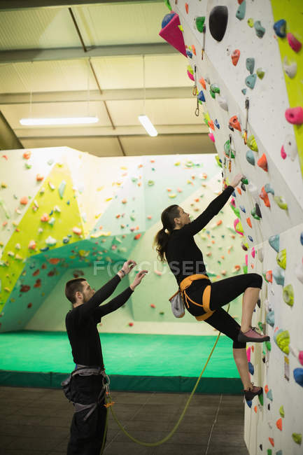 Trainer assisting woman while climbing on artificial wall in gym — Stock Photo