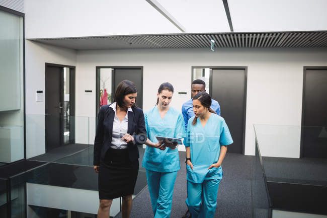 Médico y enfermeras discutiendo sobre la tableta digital mientras camina en el pasillo del hospital - foto de stock