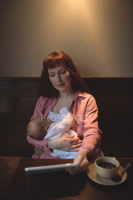 Madre con el bebé usando el teléfono móvil en la cafetería - foto de stock