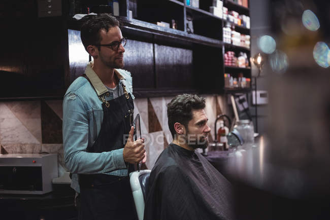 Peluquero mostrando corte de pelo hombre en el espejo en la peluquería - foto de stock