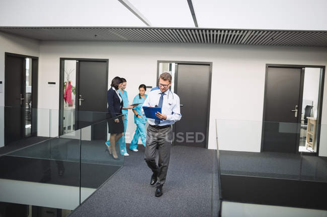 Médico mirando el informe médico mientras camina en el pasillo del hospital - foto de stock