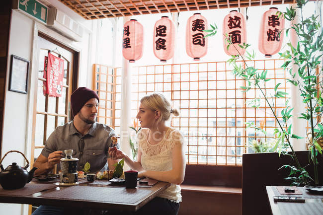 Pareja interactuando entre sí mientras toma sushi en el restaurante - foto de stock