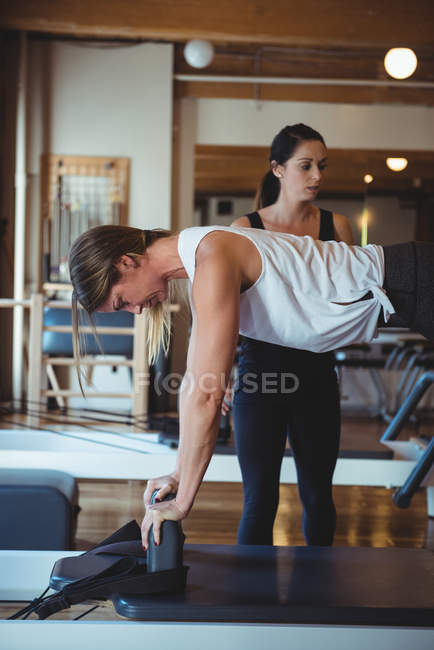 Entrenador ayudando a una mujer mientras practica pilates en el gimnasio - foto de stock