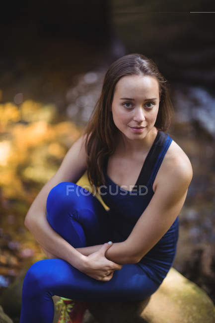 Donna sorridente seduta sulla roccia nella foresta — Foto stock