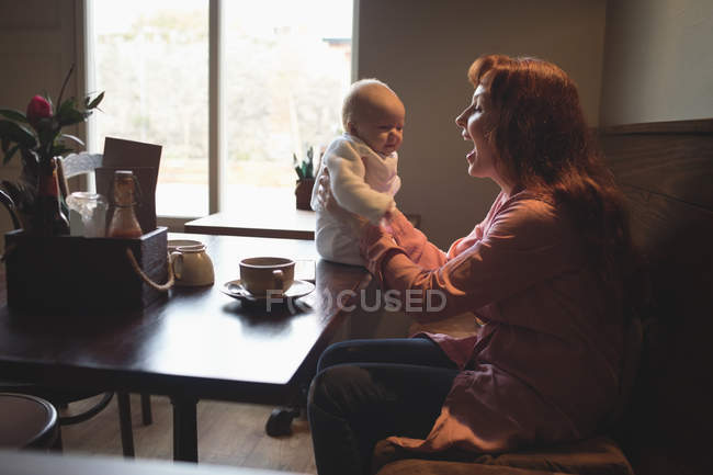 Mãe feliz brincando com o bebê no interior do café — Fotografia de Stock