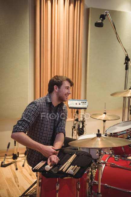 Улыбающийся барабанщик, сидящий рядом с барабанной установкой в записи музыки — стоковое фото