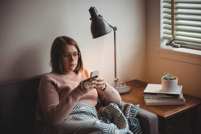 Femme assise sur un canapé utilisant un téléphone portable à la maison — Photo de stock