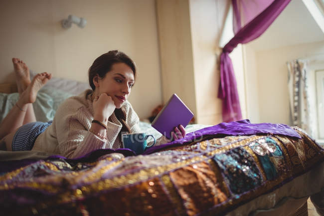 Schöne Frau mit digitalem Tablet beim Kaffee zu Hause im Bett — Stockfoto