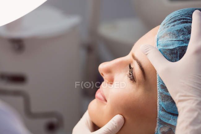 Hands of doctor examining female face for cosmetic treatment at clinic — Stock Photo