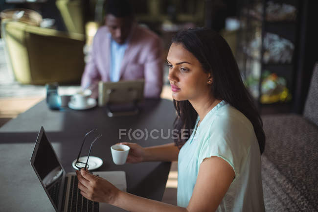 Thoughtful businesswoman holding coffee cup sitting at her desk in office — Stock Photo
