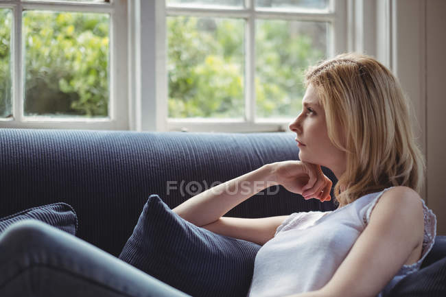 Femme réfléchie assise sur le canapé dans le salon à la maison — Photo de stock