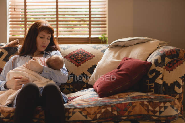 Mother breastfeeding infant baby on sofa in living room — Stock Photo